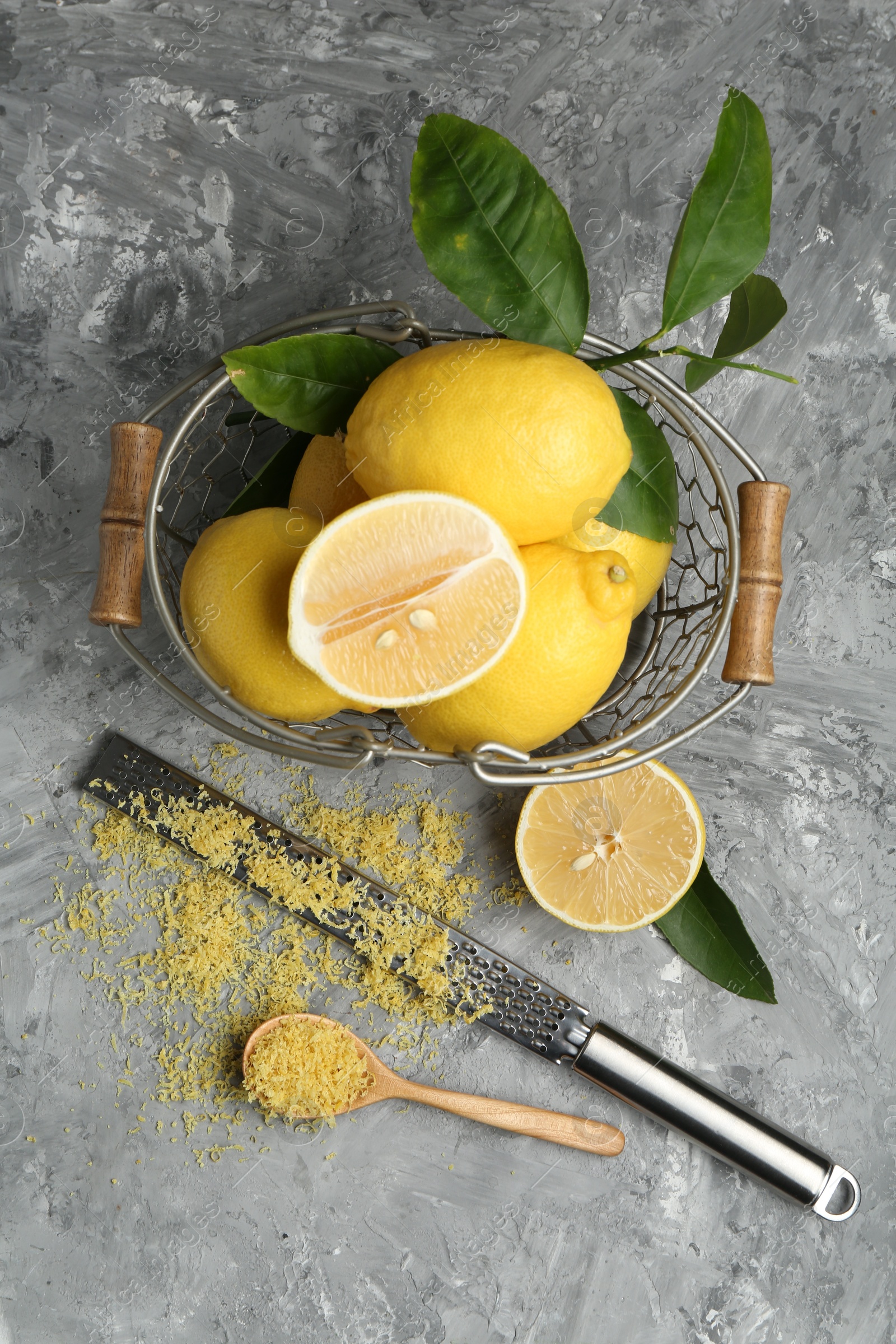 Photo of Lemon zest, spoon, grater and fresh fruits on grey textured table, top view