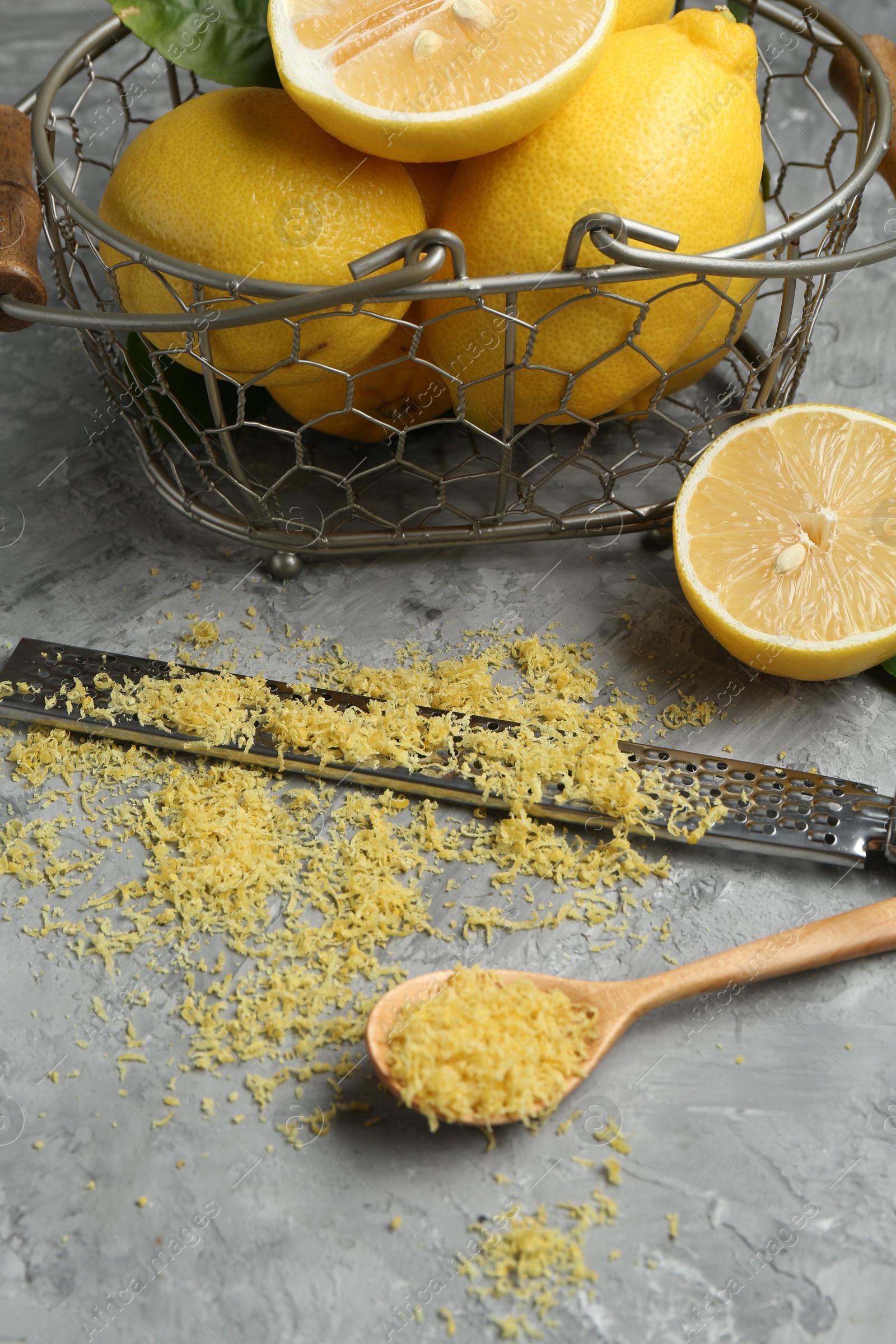 Photo of Lemon zest, spoon, grater and fresh fruits on grey textured table