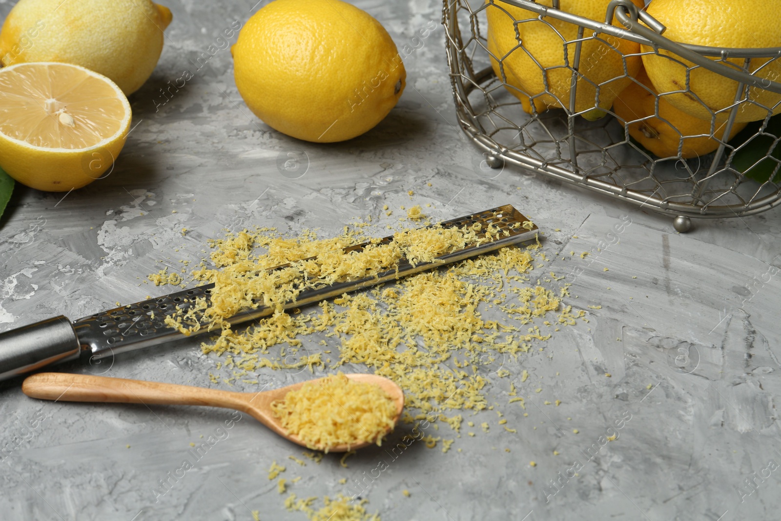 Photo of Lemon zest, spoon, grater and fresh fruits on grey textured table