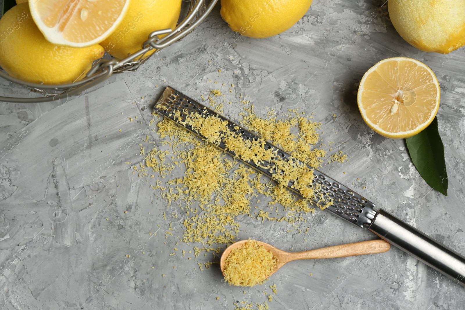 Photo of Lemon zest, spoon, grater and fresh fruits on grey textured table, flat lay