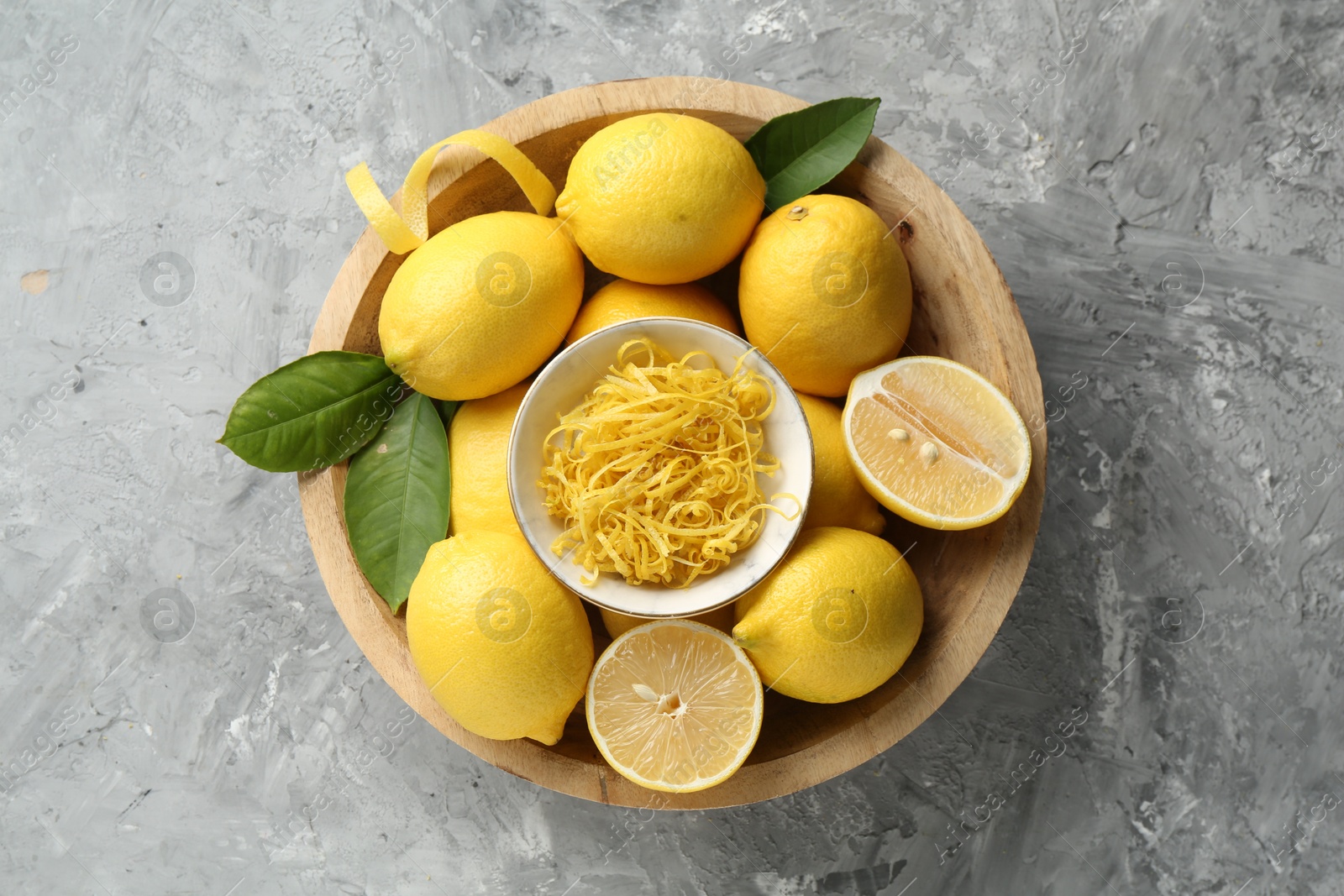 Photo of Lemon zest and fresh fruits in bowl on grey textured table, top view