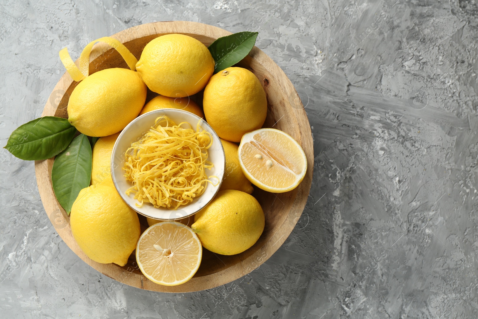 Photo of Lemon zest and fresh fruits in bowl on grey textured table, top view