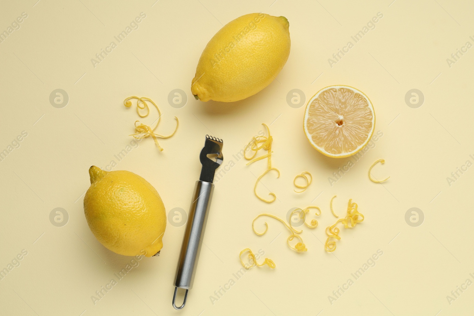 Photo of Lemon zest, zester tool and fresh fruits on beige background, flat lay