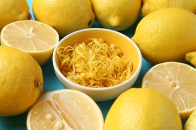 Photo of Lemon zest in bowl and fresh fruits on light blue background, closeup