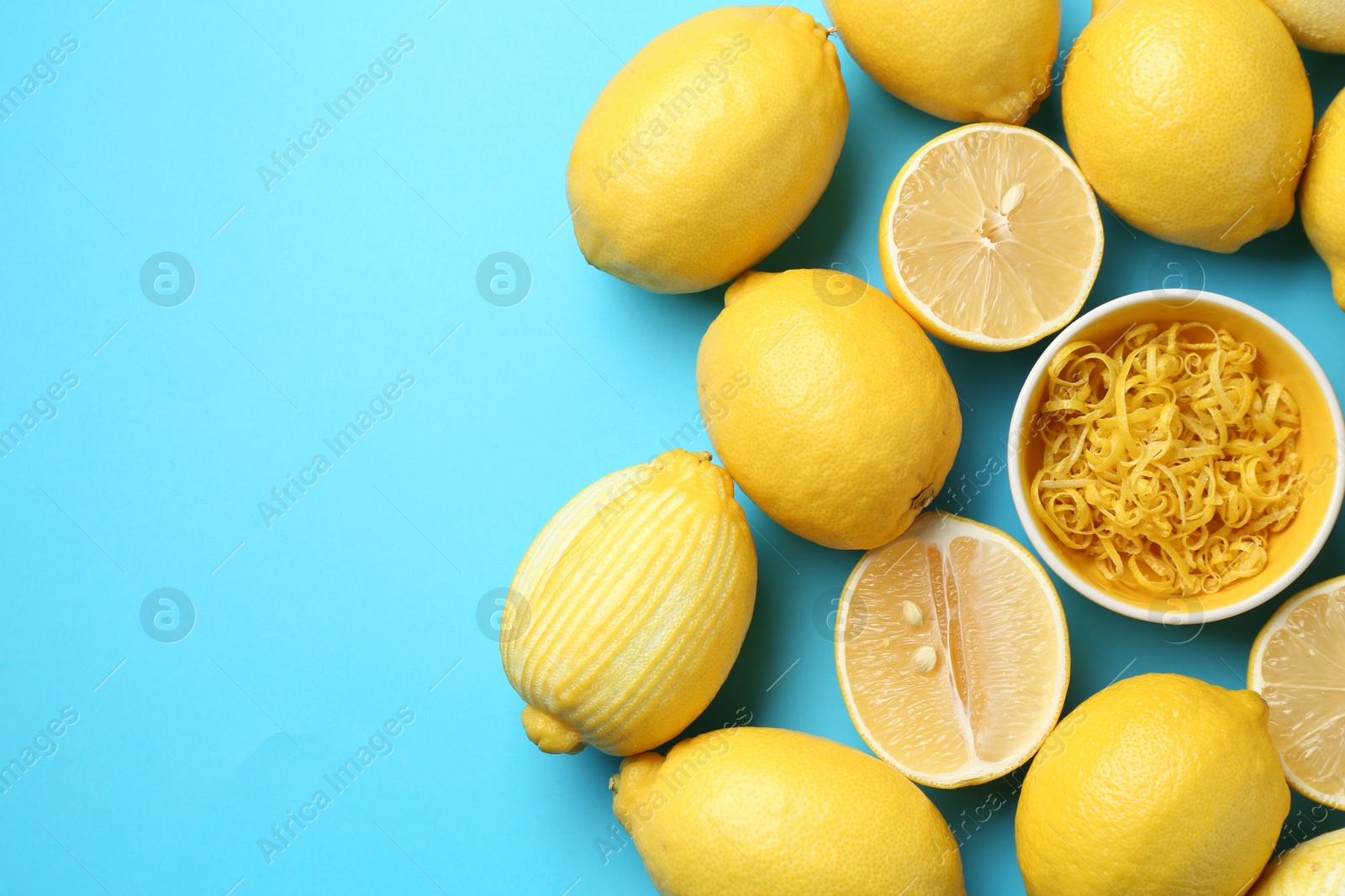 Photo of Lemon zest in bowl and fresh fruits on light blue background, top view. Space for text