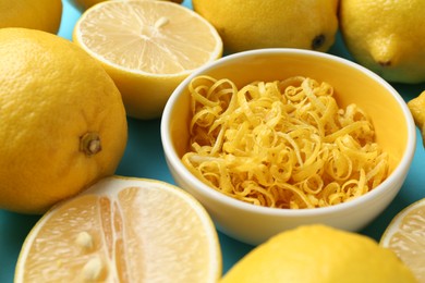 Photo of Lemon zest in bowl and fresh fruits on light blue background, closeup