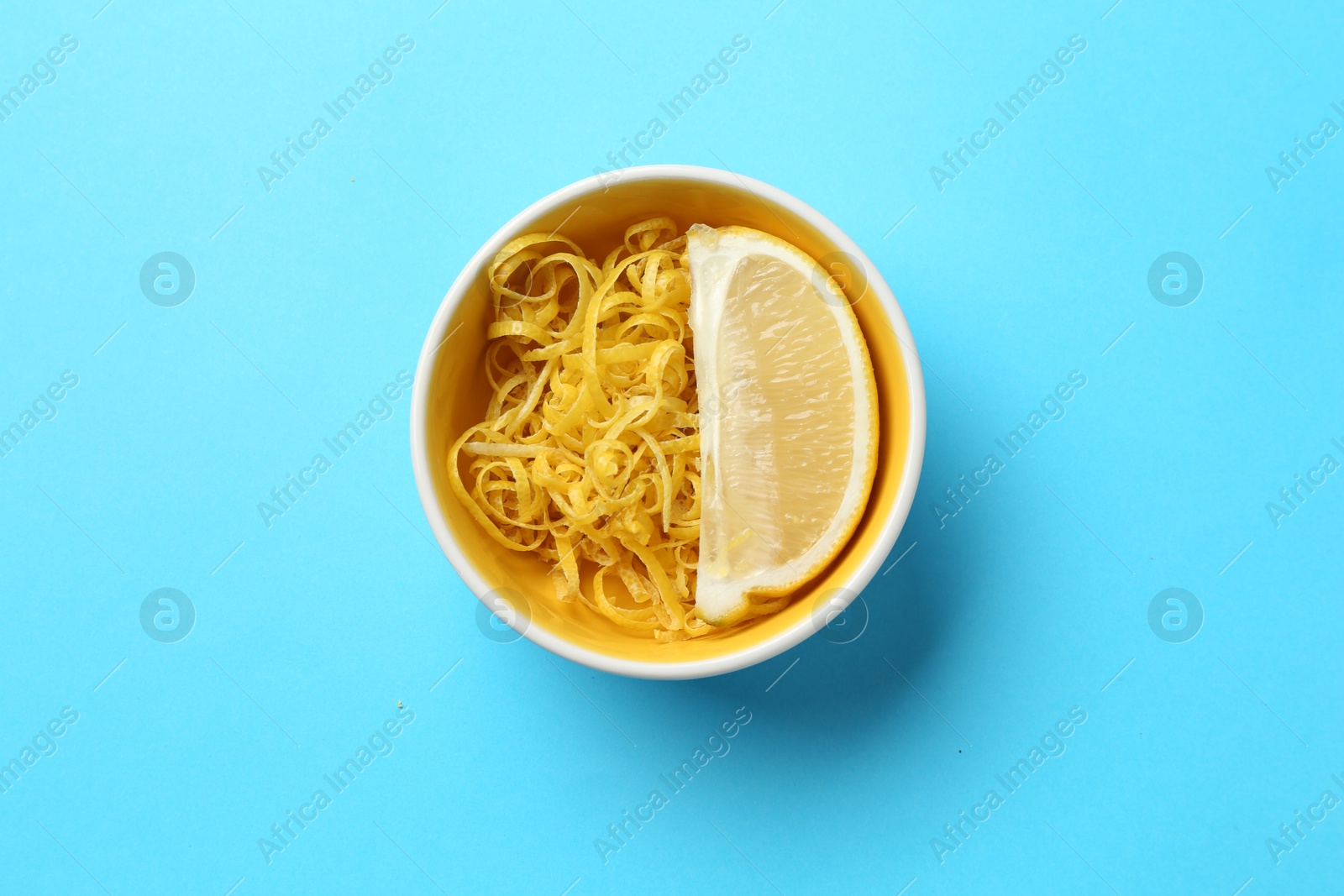 Photo of Lemon zest and piece of fresh fruit on light blue background, top view