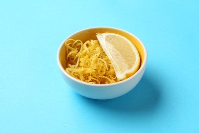 Photo of Lemon zest and piece of fresh fruit on light blue background, closeup