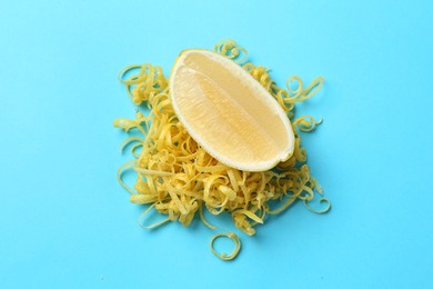 Photo of Lemon zest and piece of fresh fruit on light blue background, top view