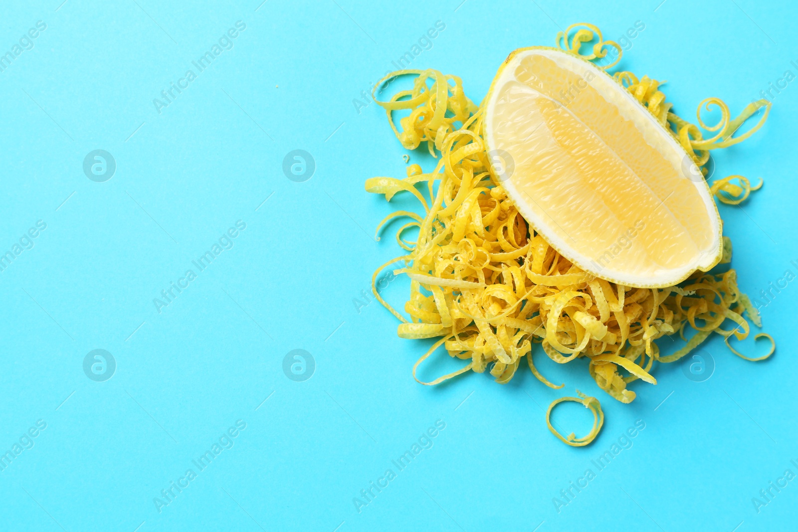 Photo of Lemon zest and piece of fresh fruit on light blue background, top view. Space for text