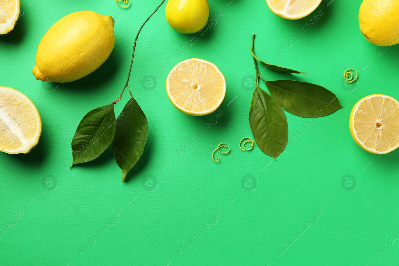 Photo of Lemon zest, fresh fruits and leaves on green background, flat lay. Space for text