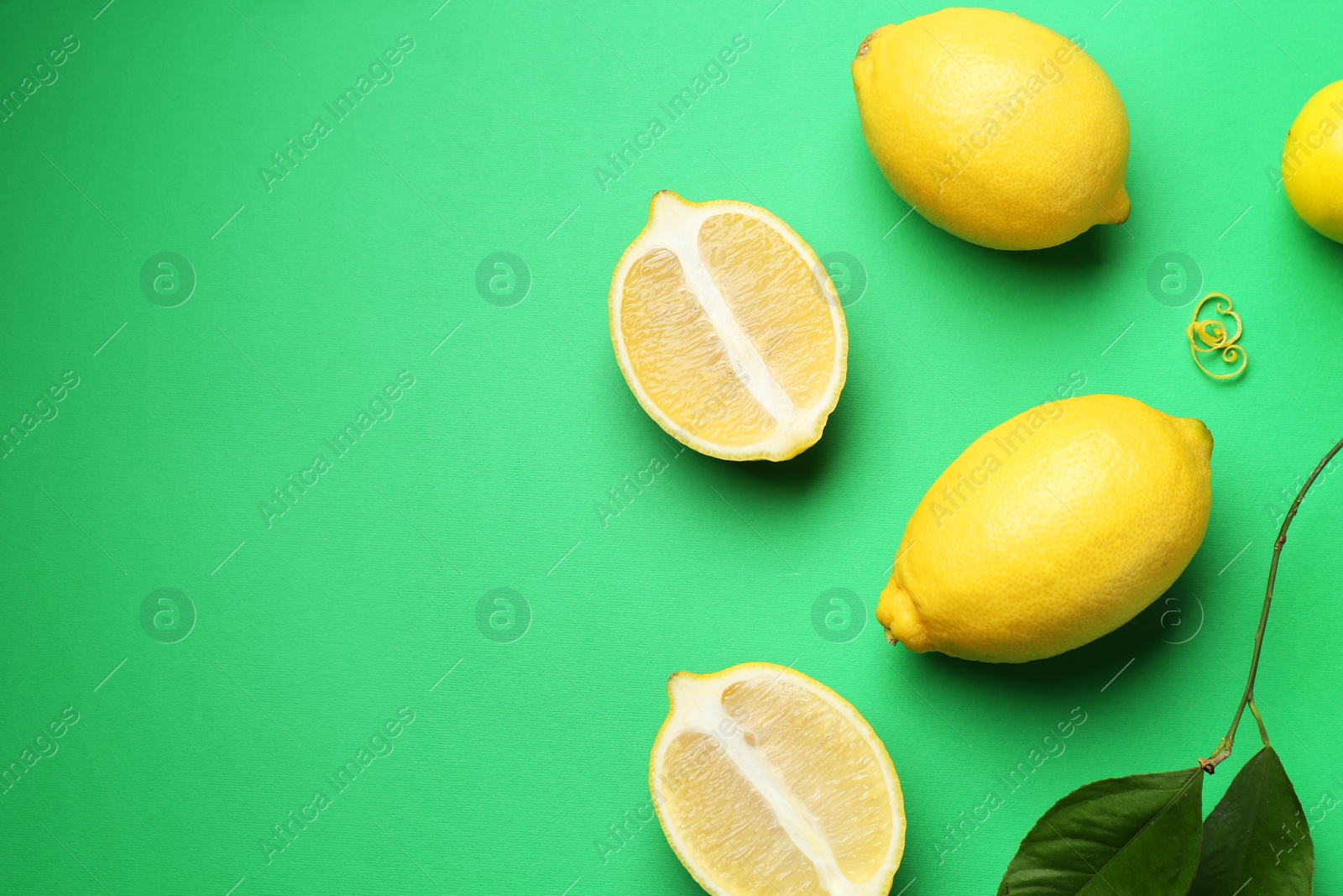 Photo of Lemon zest, fresh fruits and leaves on green background, flat lay. Space for text