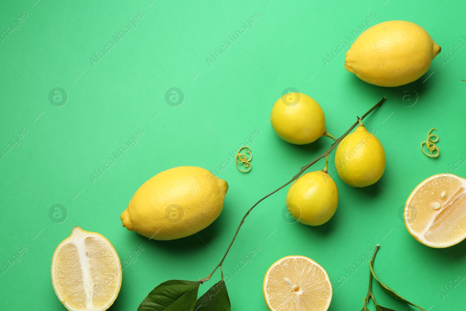 Photo of Lemon zest, fresh fruits and leaves on green background, flat lay. Space for text