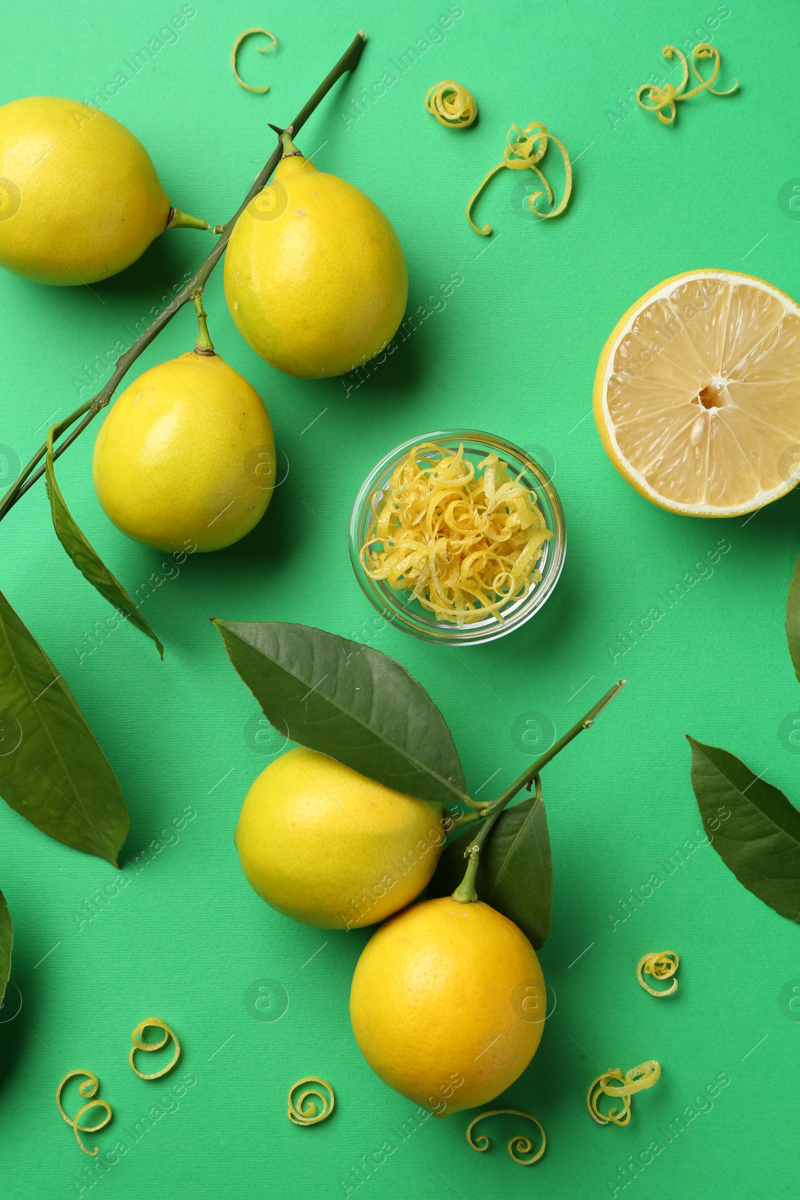 Photo of Lemon zest, fresh fruits and leaves on green background, flat lay