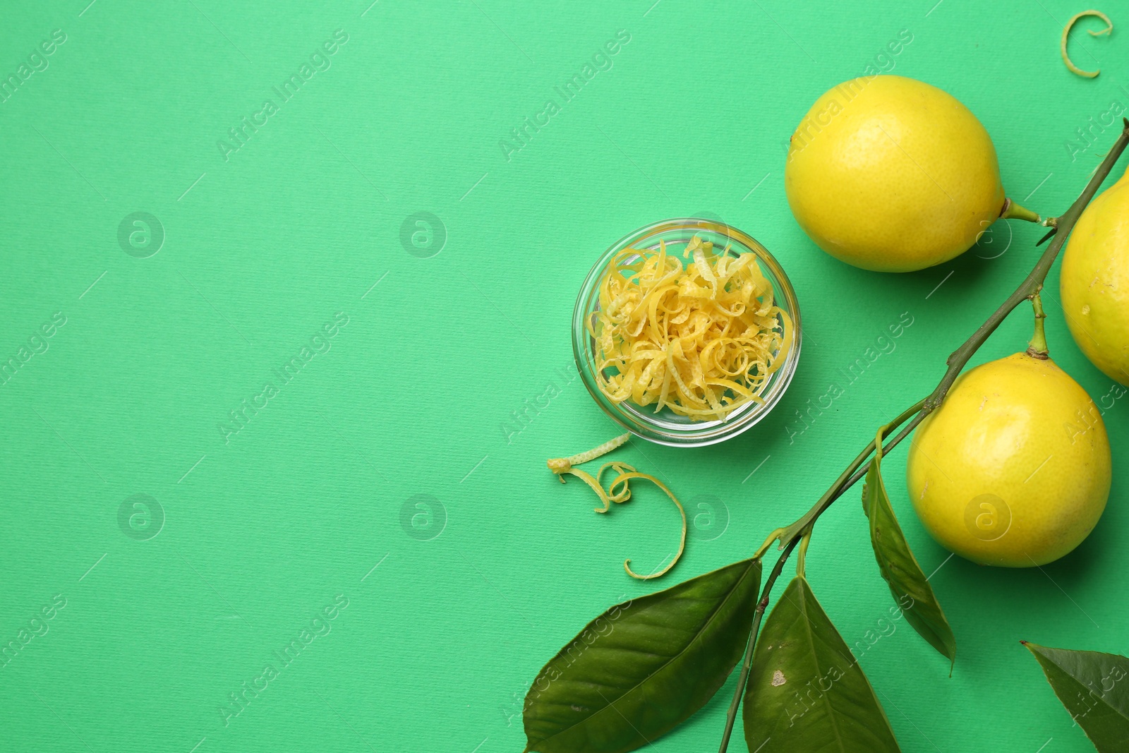 Photo of Lemon zest, fresh fruits and leaves on green background, flat lay. Space for text