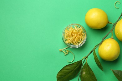 Photo of Lemon zest, fresh fruits and leaves on green background, flat lay. Space for text