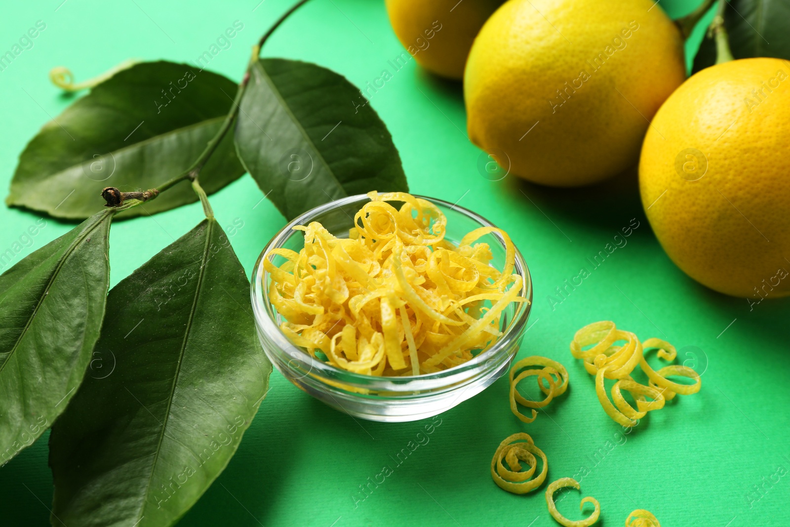 Photo of Lemon zest, fresh fruits and leaves on green background, closeup