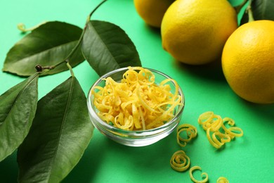 Photo of Lemon zest, fresh fruits and leaves on green background, closeup