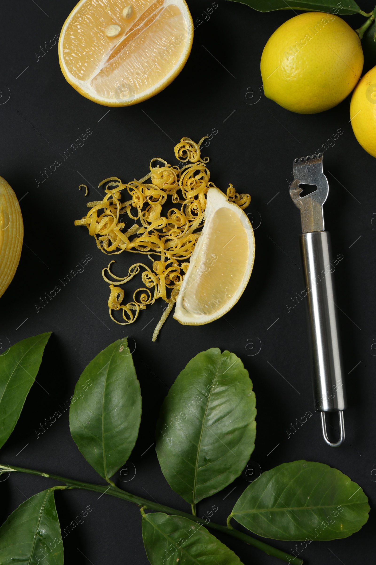 Photo of Lemon zest, zester tool, fresh fruits and leaves on black background, flat lay