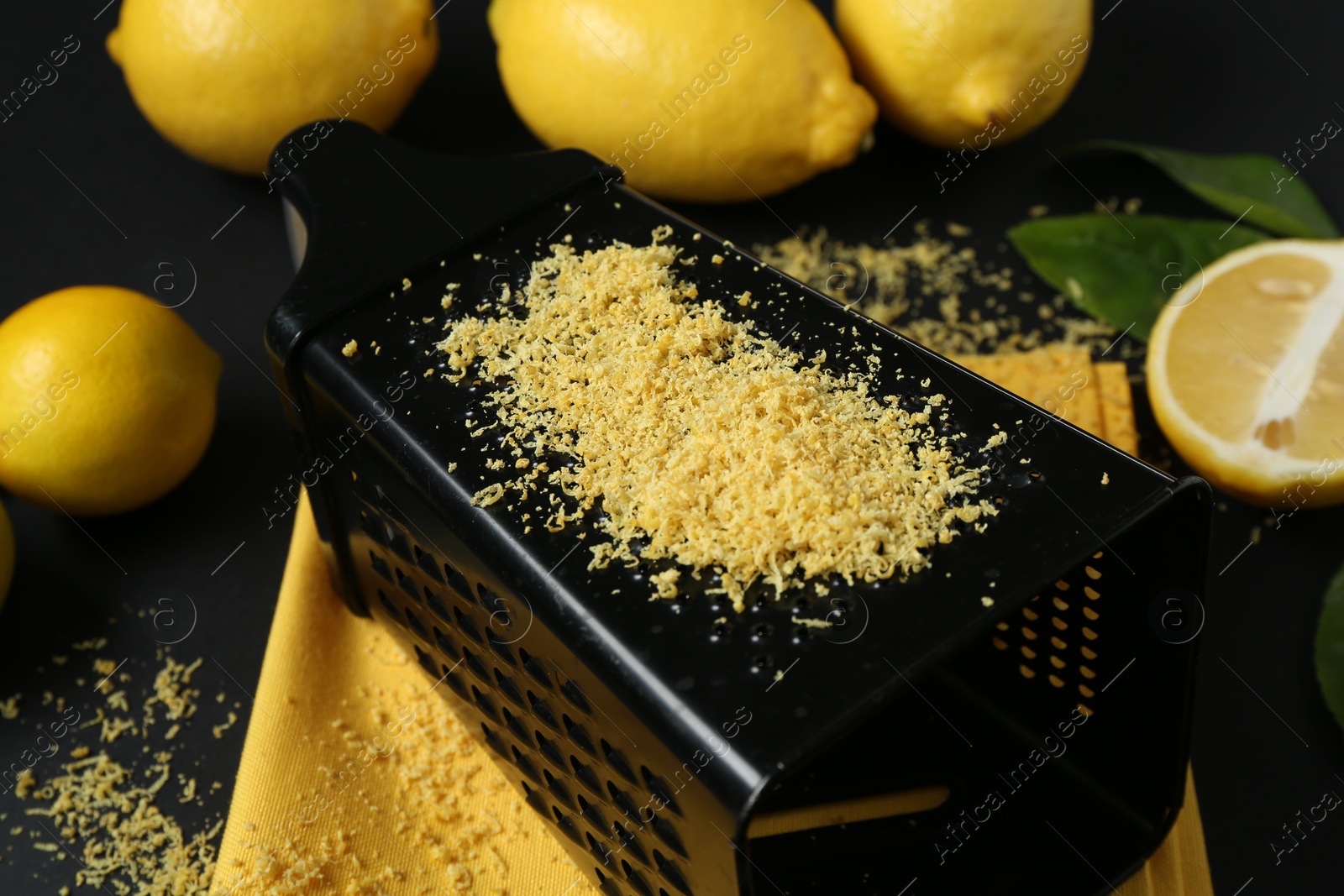 Photo of Grater with lemon zest, fresh fruits and leaves on black background, closeup