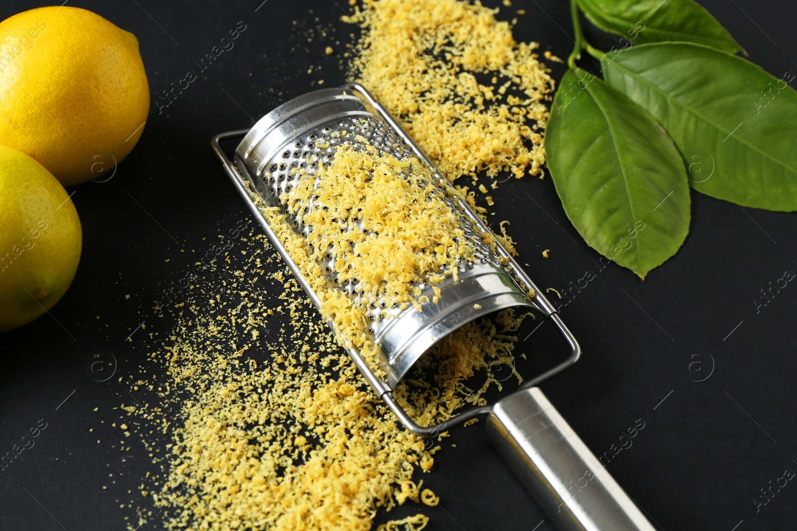 Photo of Grater with lemon zest, fresh fruits and leaves on black background, closeup