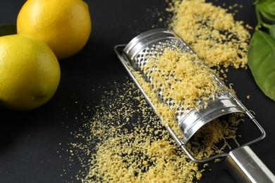 Photo of Grater with lemon zest, fresh fruits and leaves on black background, closeup