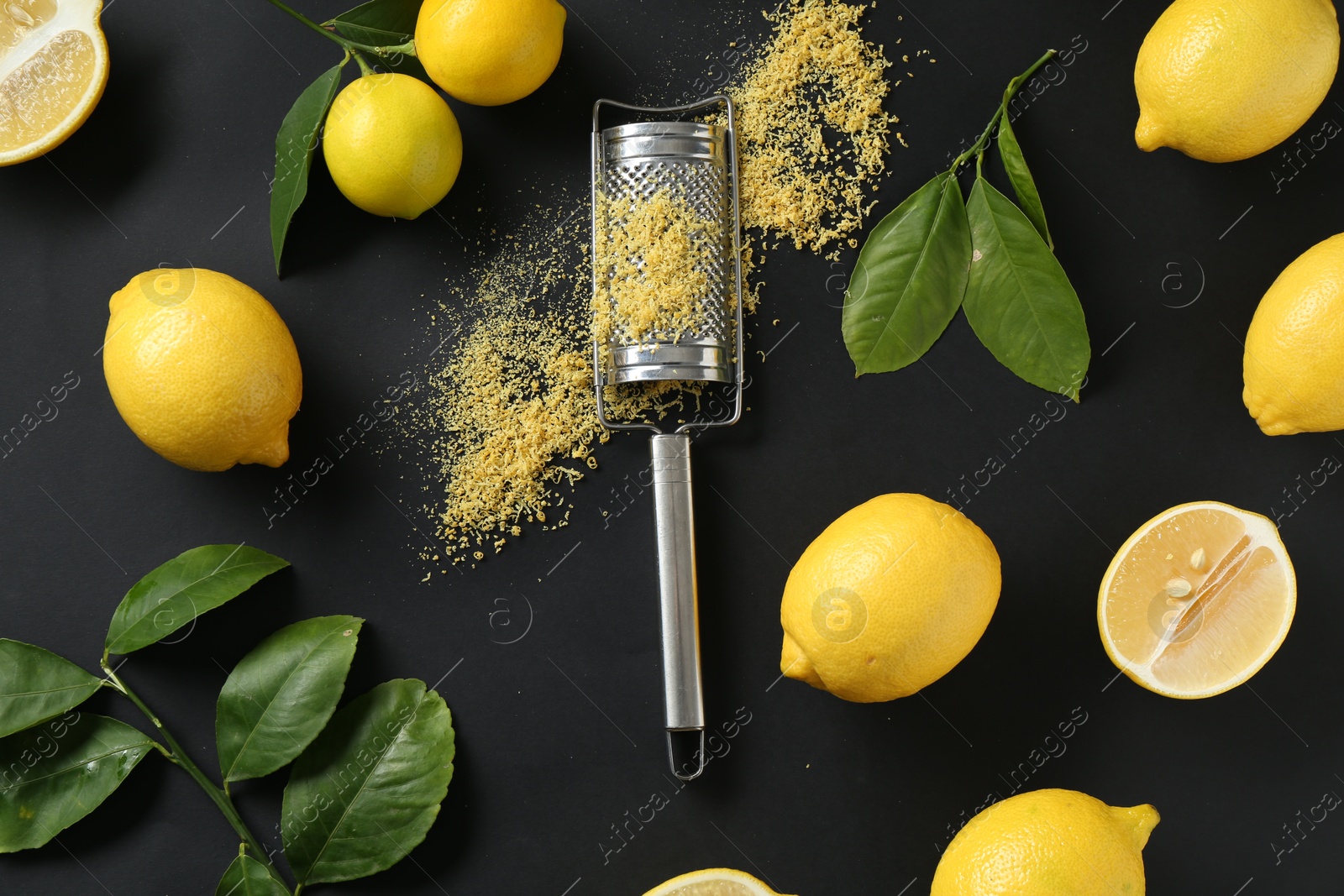 Photo of Grater with lemon zest, fresh fruits and leaves on black background, flat lay