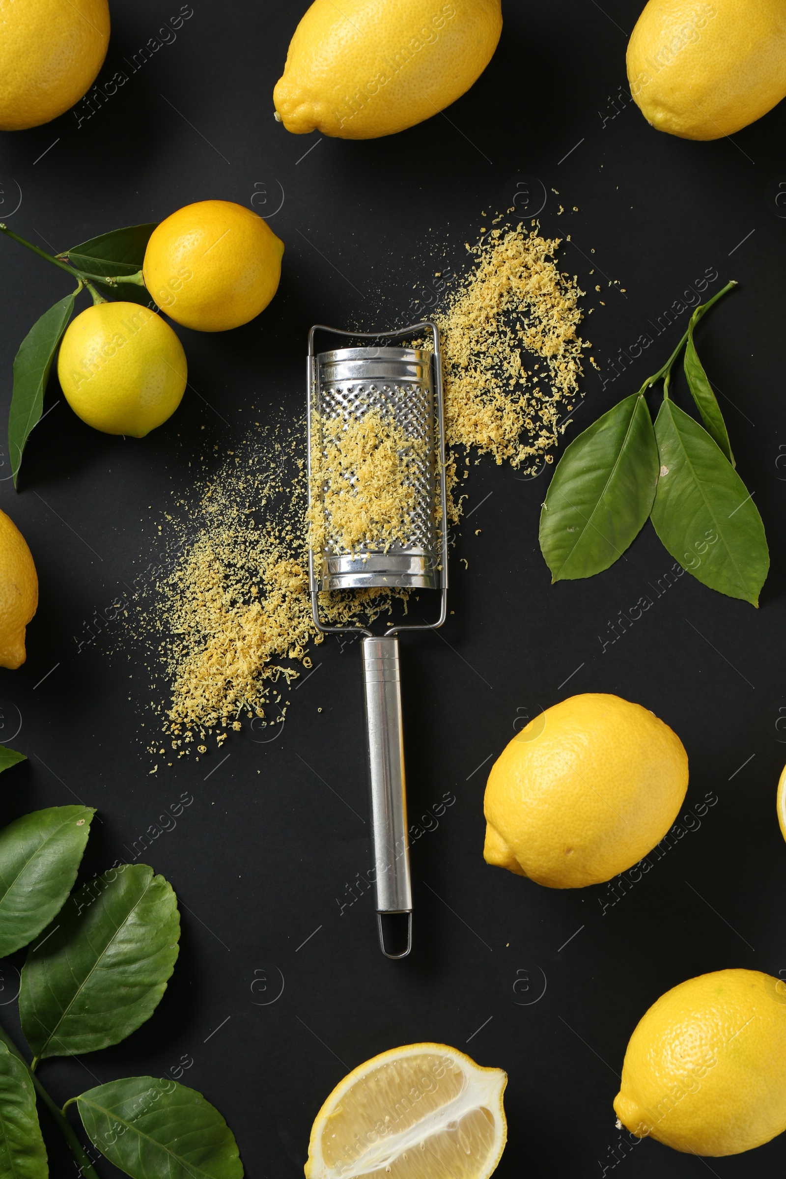 Photo of Grater with lemon zest, fresh fruits and leaves on black background, flat lay