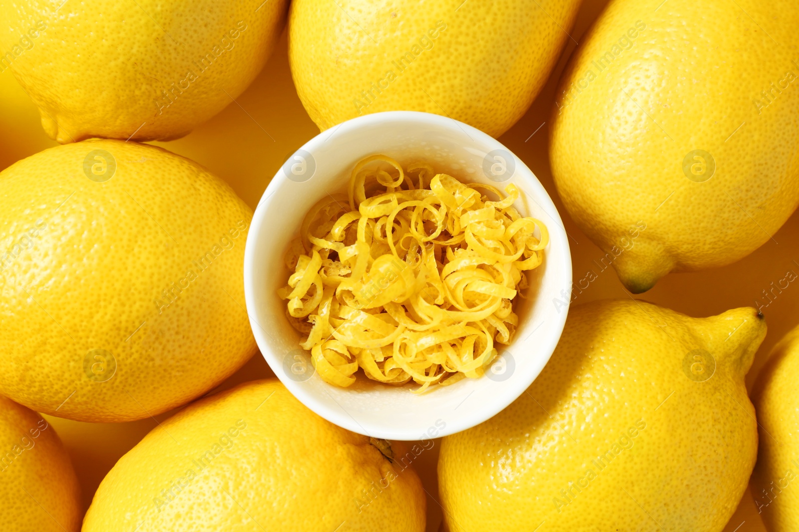 Photo of Lemon zest in bowl and fresh fruits on yellow background, top view