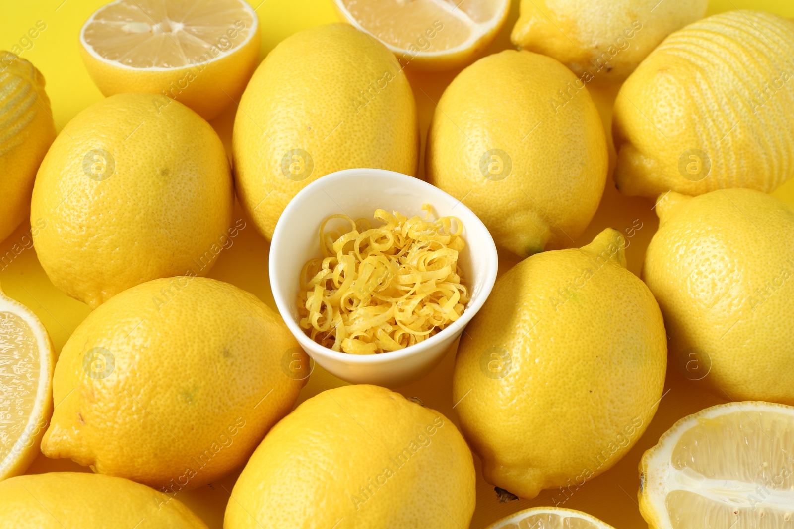 Photo of Lemon zest in bowl and fresh fruits on yellow background, closeup