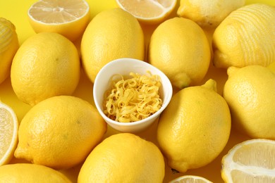 Photo of Lemon zest in bowl and fresh fruits on yellow background, closeup