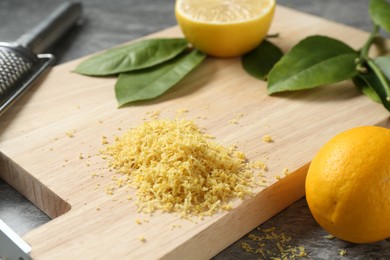 Photo of Lemon zest, grater and fresh fruits on grey textured table, closeup