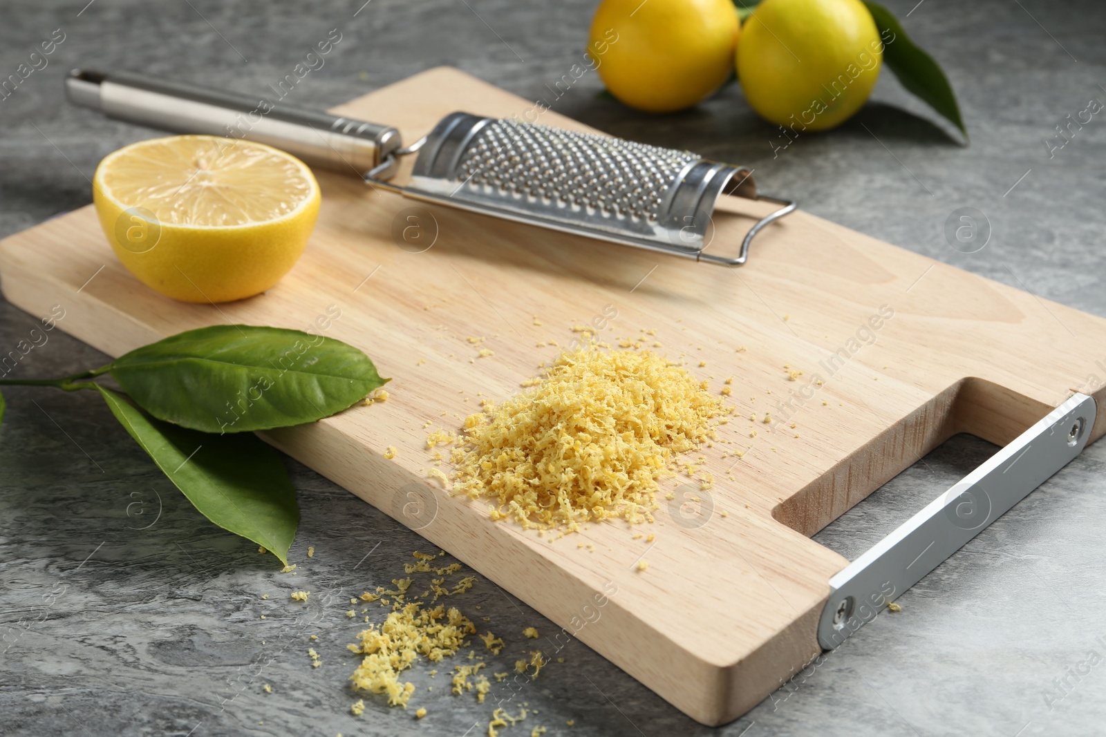 Photo of Lemon zest, grater and fresh fruits on grey textured table, closeup