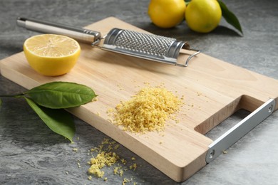 Photo of Lemon zest, grater and fresh fruits on grey textured table, closeup