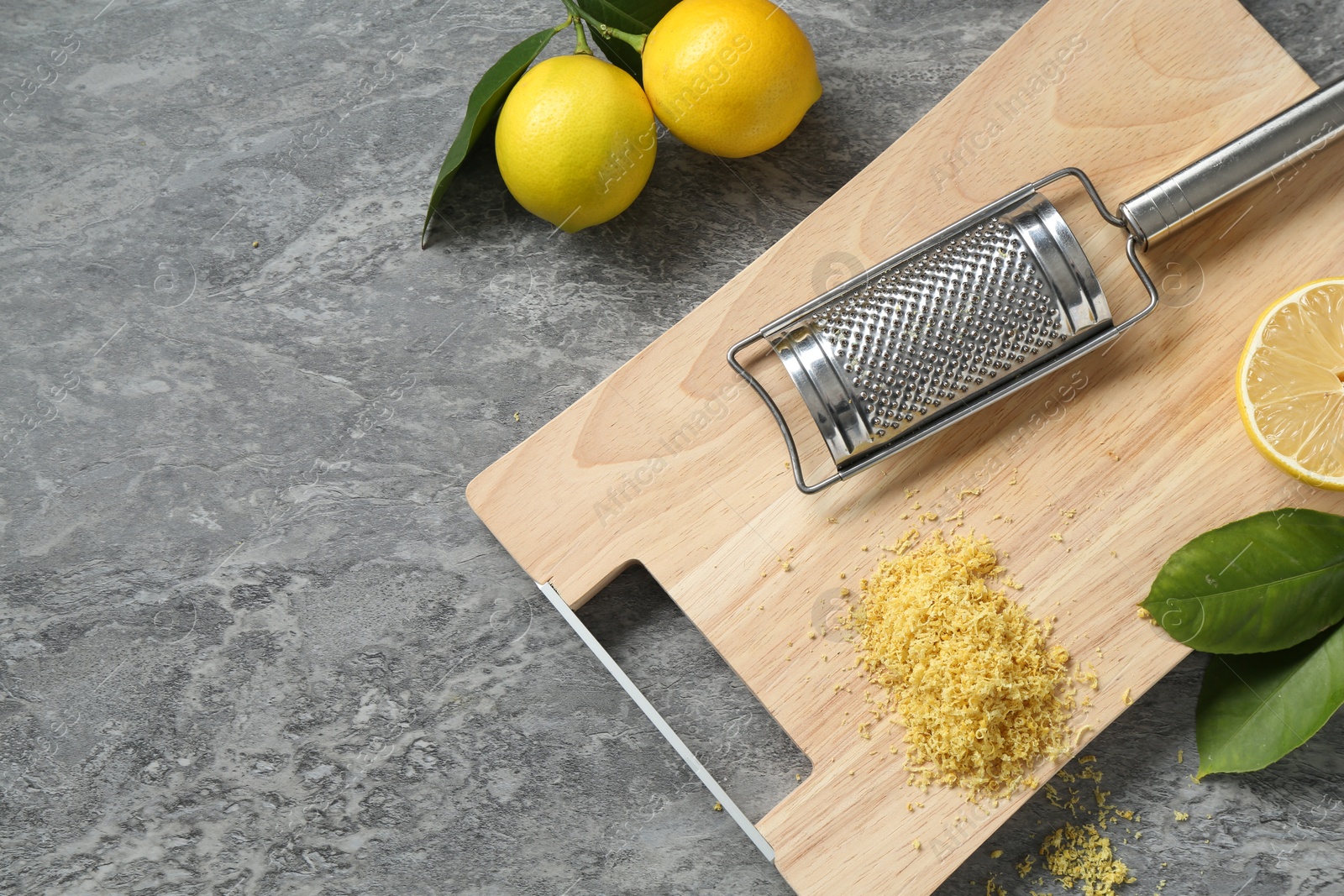 Photo of Lemon zest, grater and fresh fruits on grey textured table, top view. Space for text