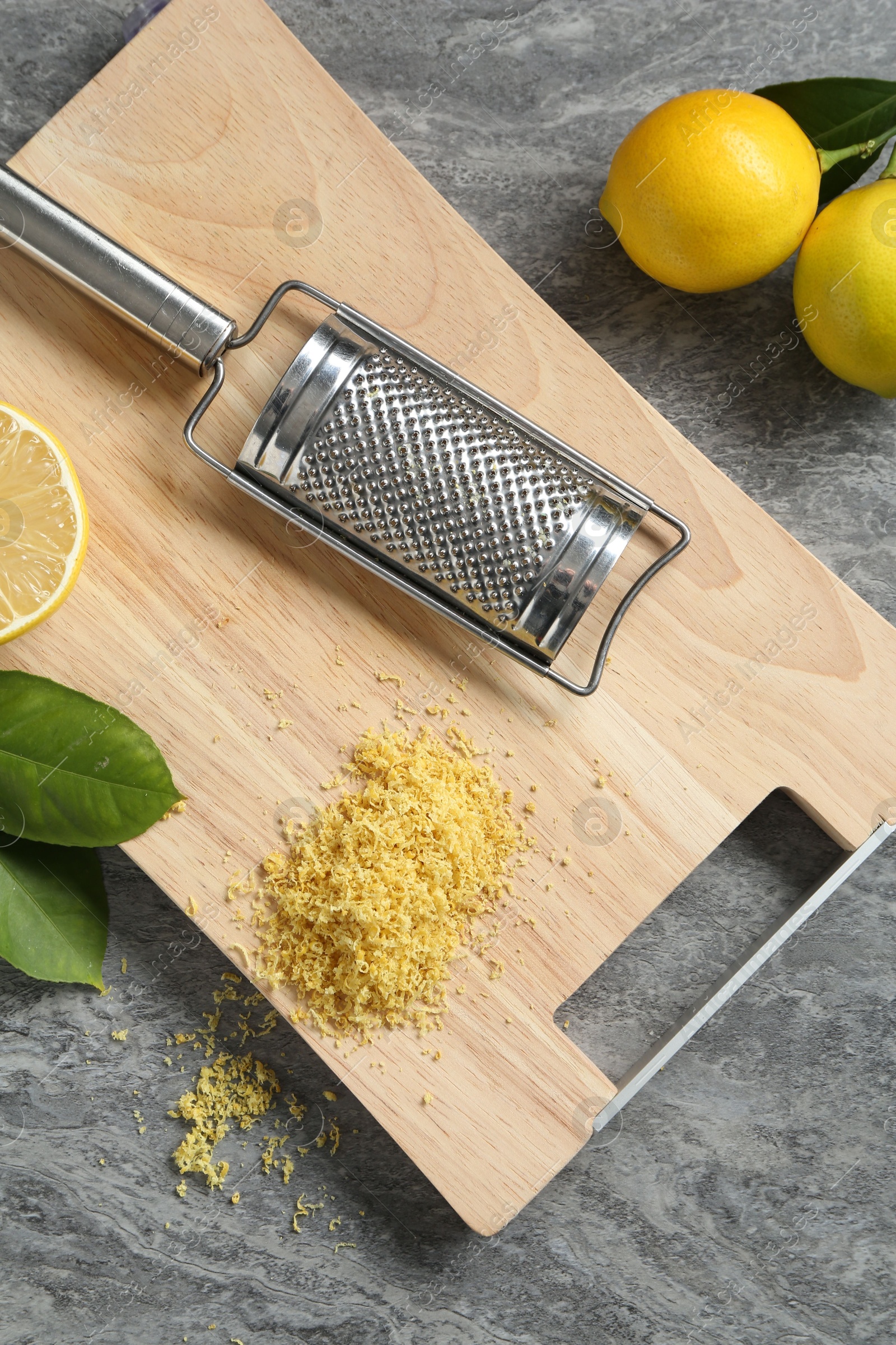 Photo of Lemon zest, grater and fresh fruits on grey textured table, top view