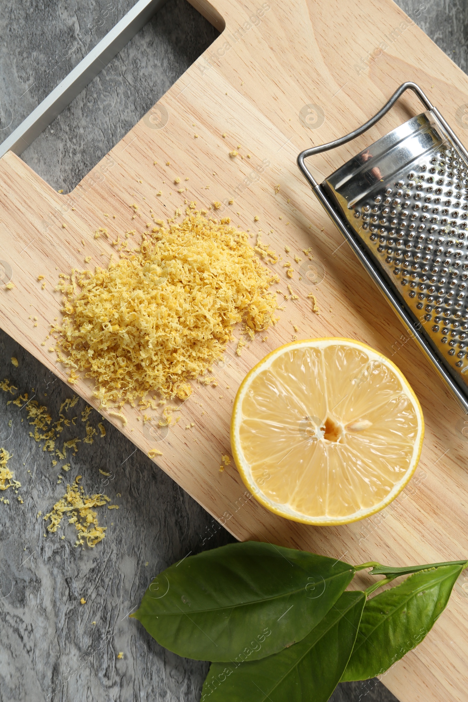 Photo of Lemon zest, grater and fresh fruits on grey textured table, top view