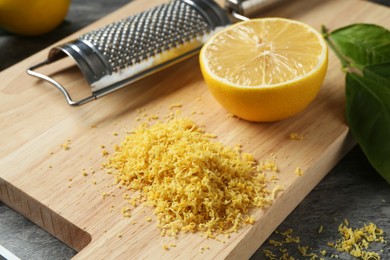 Photo of Lemon zest, grater and fresh fruits on grey textured table, closeup