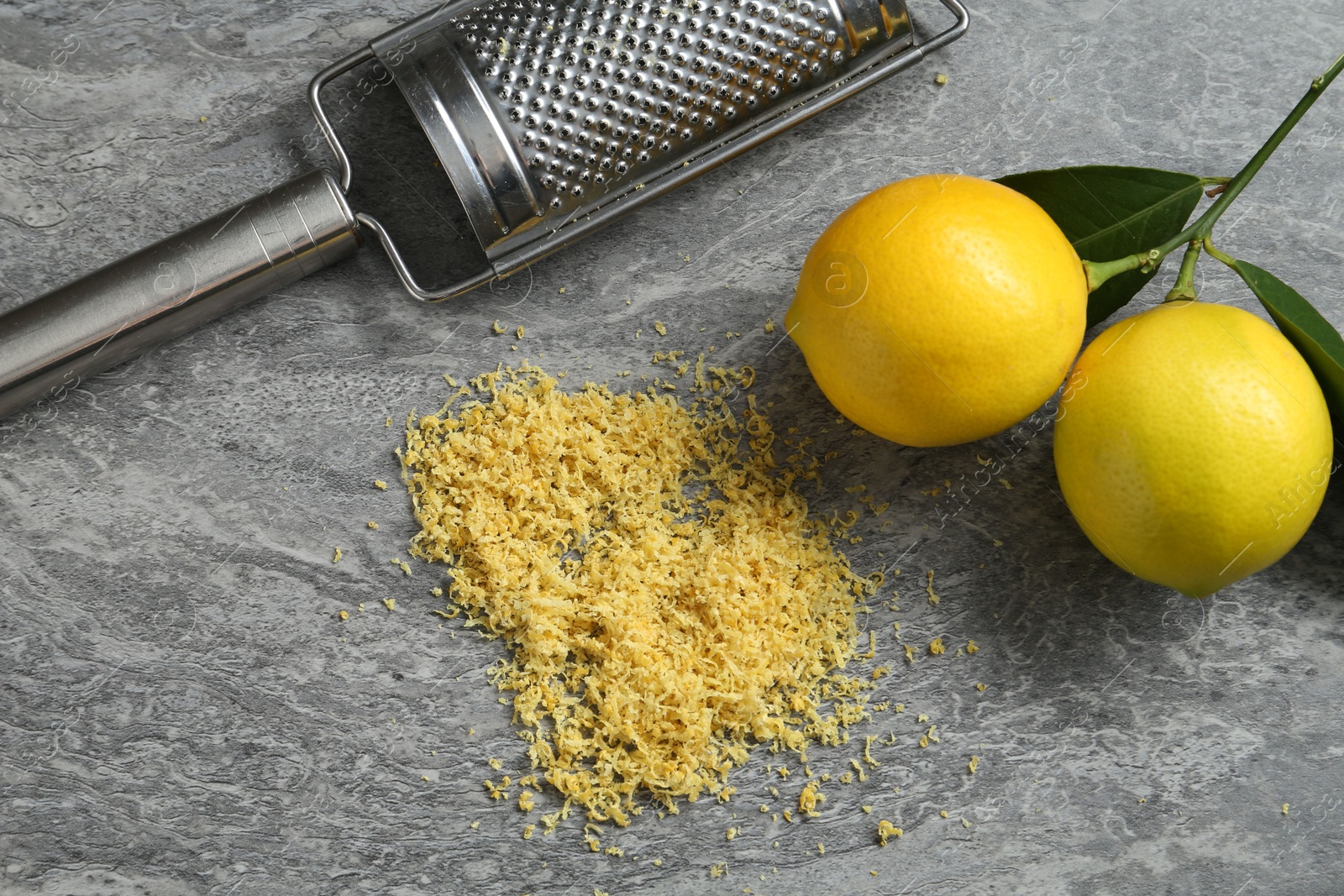 Photo of Lemon zest, grater and fresh fruits on grey textured table, flat lay