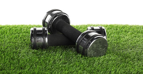 Photo of Dumbbells on artificial grass isolated on white. Sport equipment