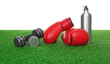 Photo of Boxing gloves, thermo bottle and dumbbells on green grass against white background. Sport equipment