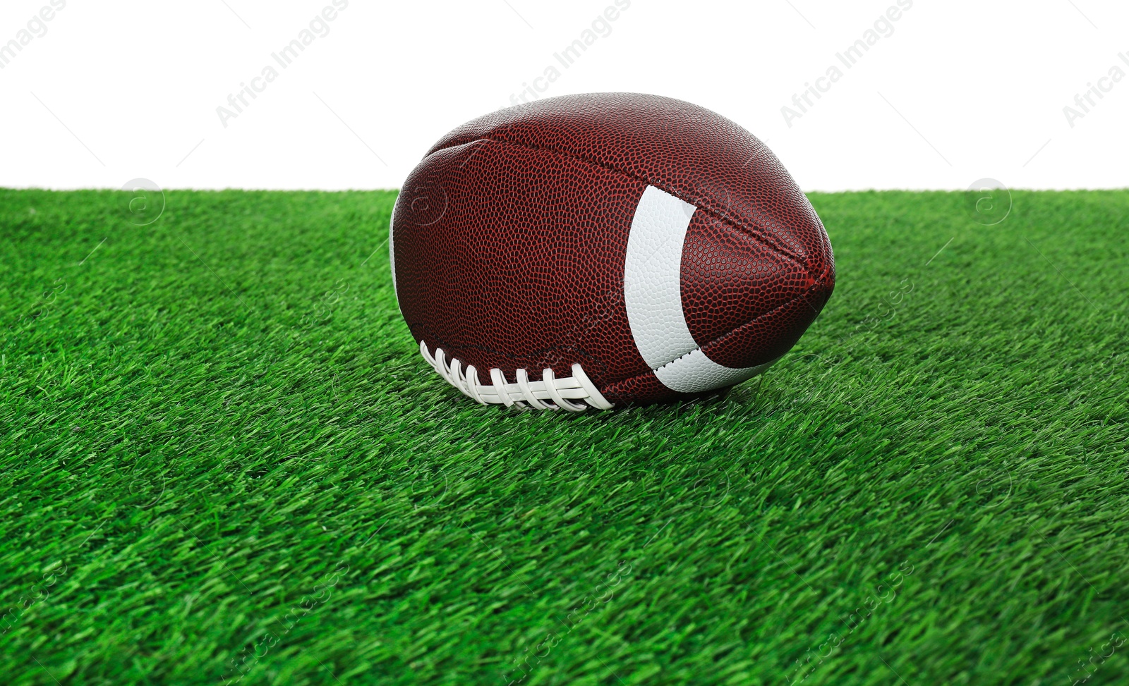 Photo of American football ball on green grass against white background. Sport equipment