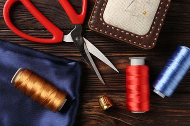 Photo of Different sewing supplies on wooden table, flat lay