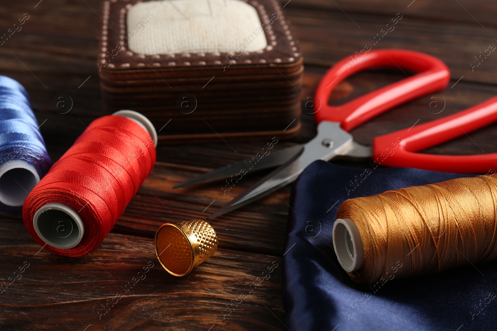 Photo of Different sewing supplies on wooden table, closeup