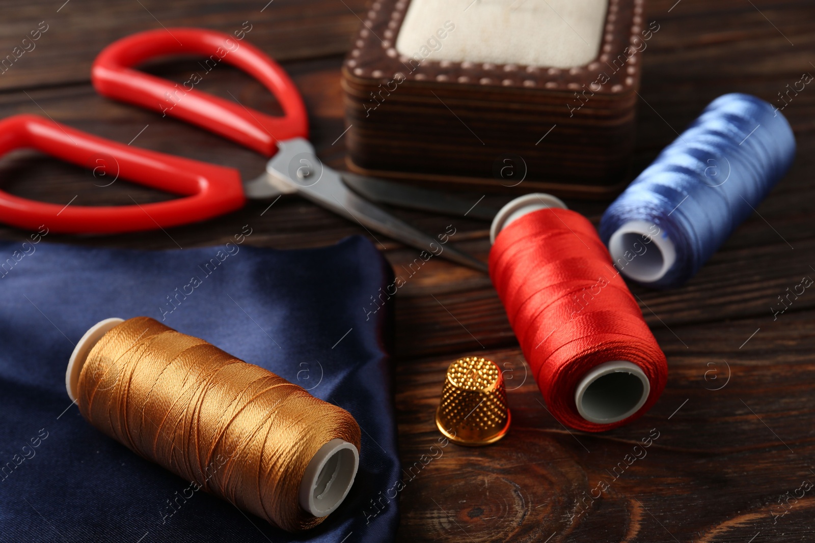 Photo of Different sewing supplies on wooden table, closeup