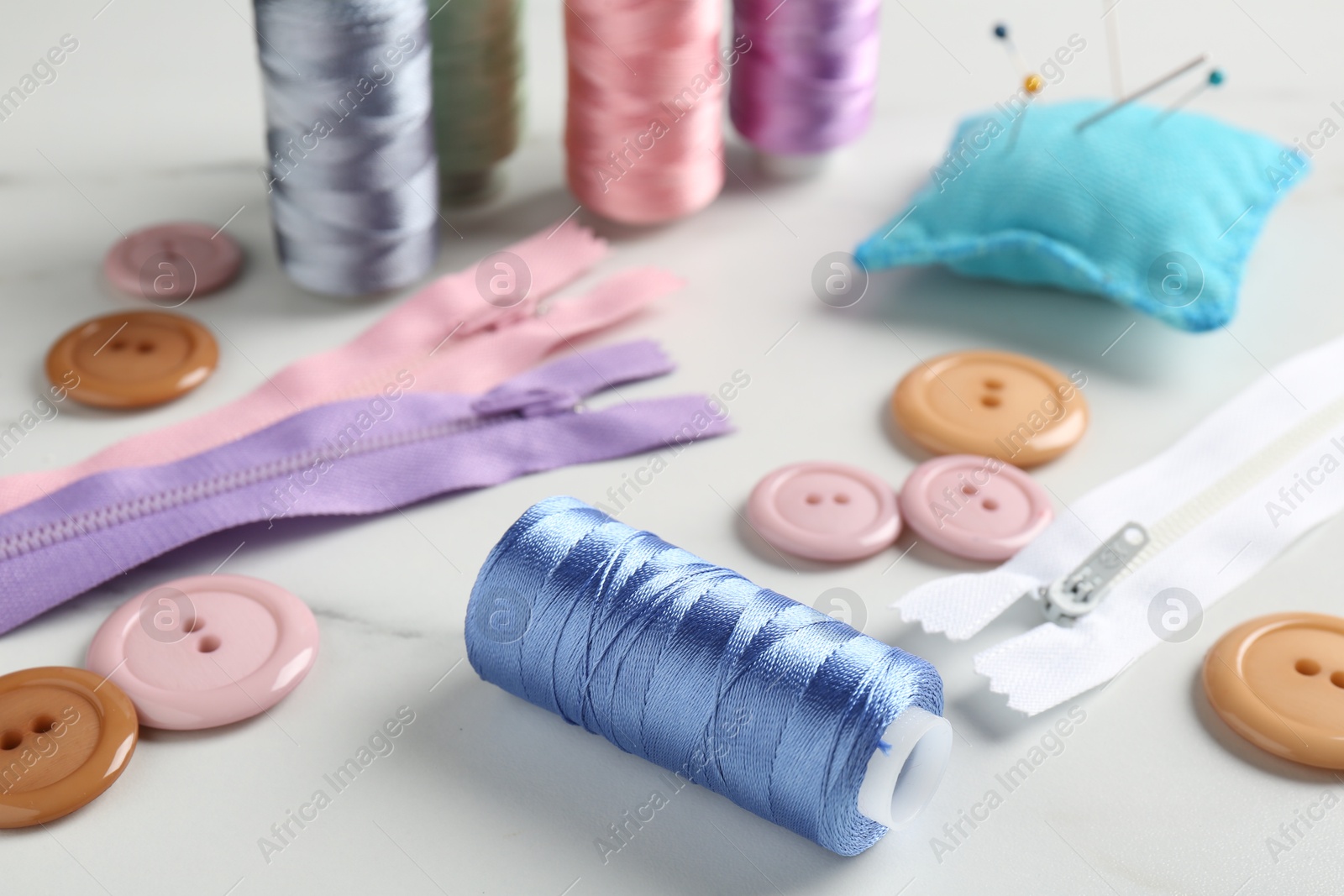 Photo of Different sewing supplies on white marble table, closeup