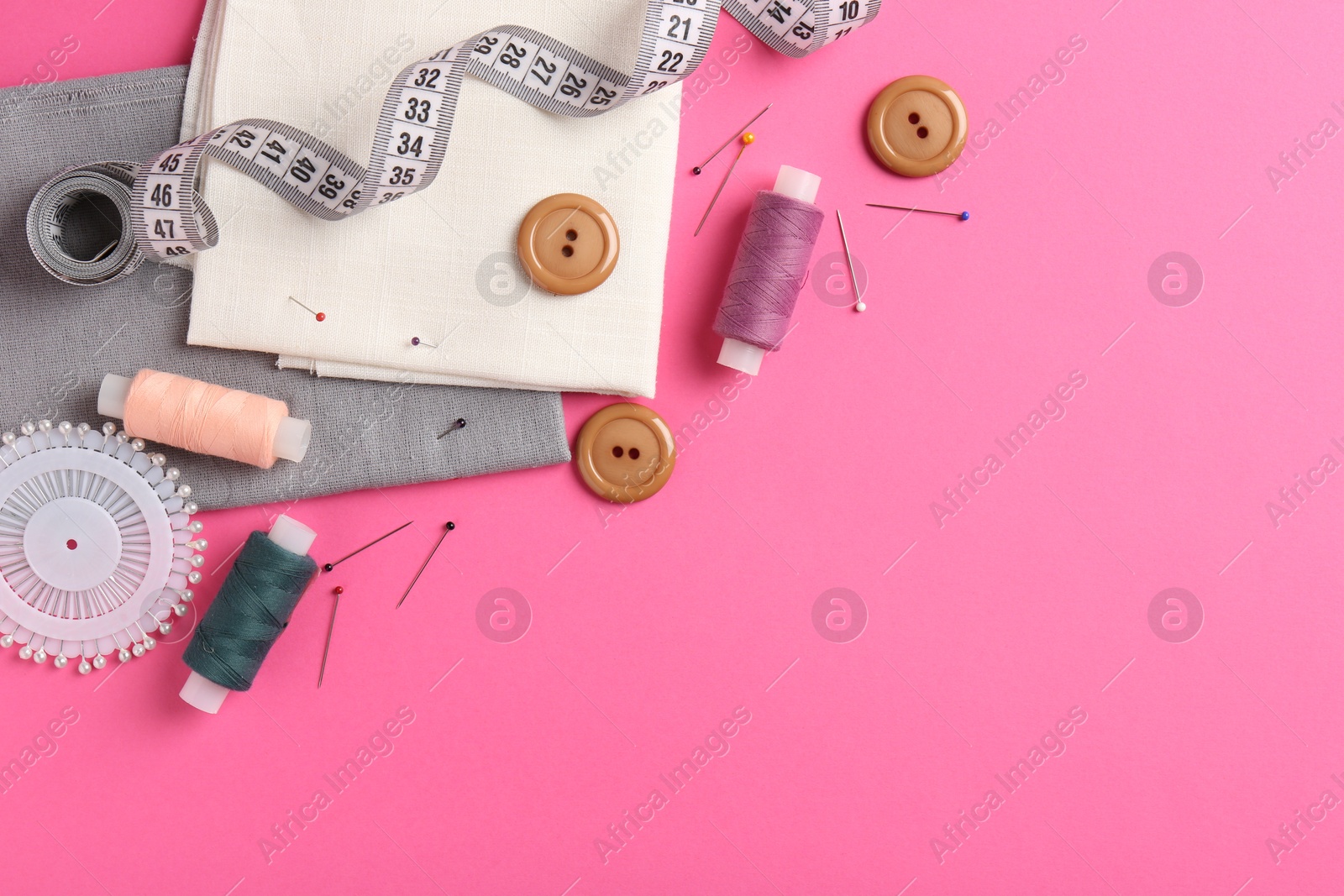 Photo of Different sewing supplies on pink background, flat lay. Space for text