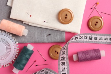 Photo of Different sewing supplies on pink background, flat lay