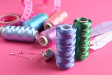 Photo of Different sewing supplies on pink background, closeup