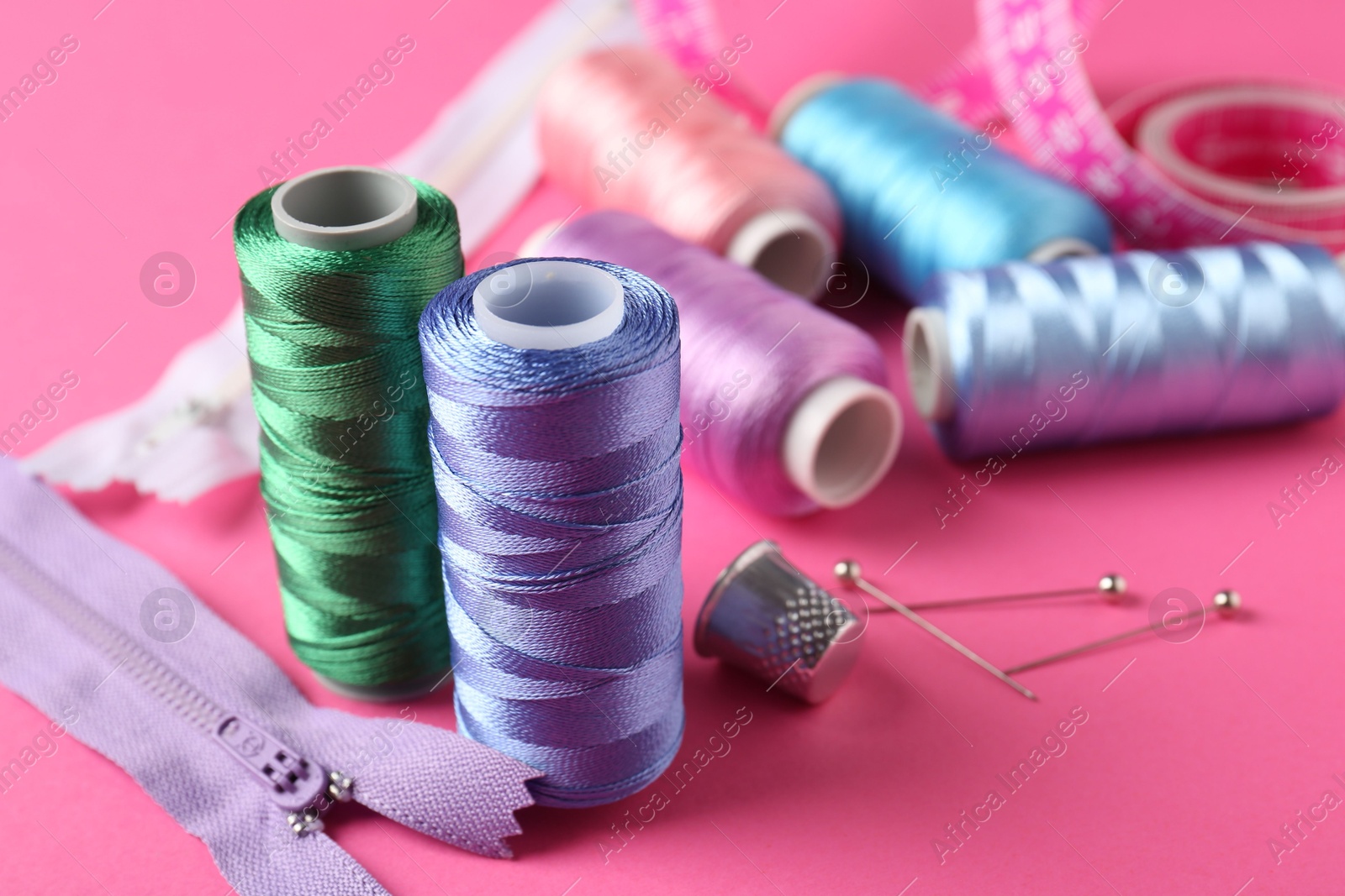 Photo of Different sewing supplies on pink background, closeup